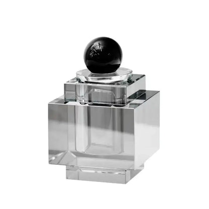 Clear acrylic perfume bottle with glossy black stopper displayed alongside geometric gold and silver crystal storage jar bedroom decor
