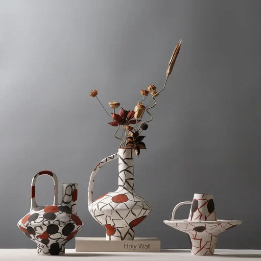 White ceramic geometric graffiti ceramic vase with black terracotta patterns and curved handle holding dried flowers
