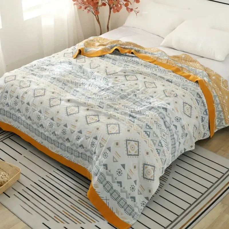 A cozy cotton gauze geometry summer throw blanket with gray and cream geometric patterns and mustard-yellow borders