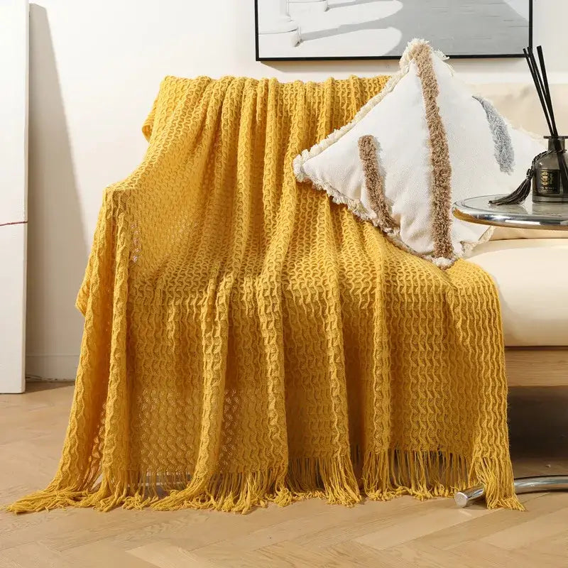 A cozy mustard-yellow geometric knit sofa blanket with textured waffle pattern and long fringe tassels for decorbites decor