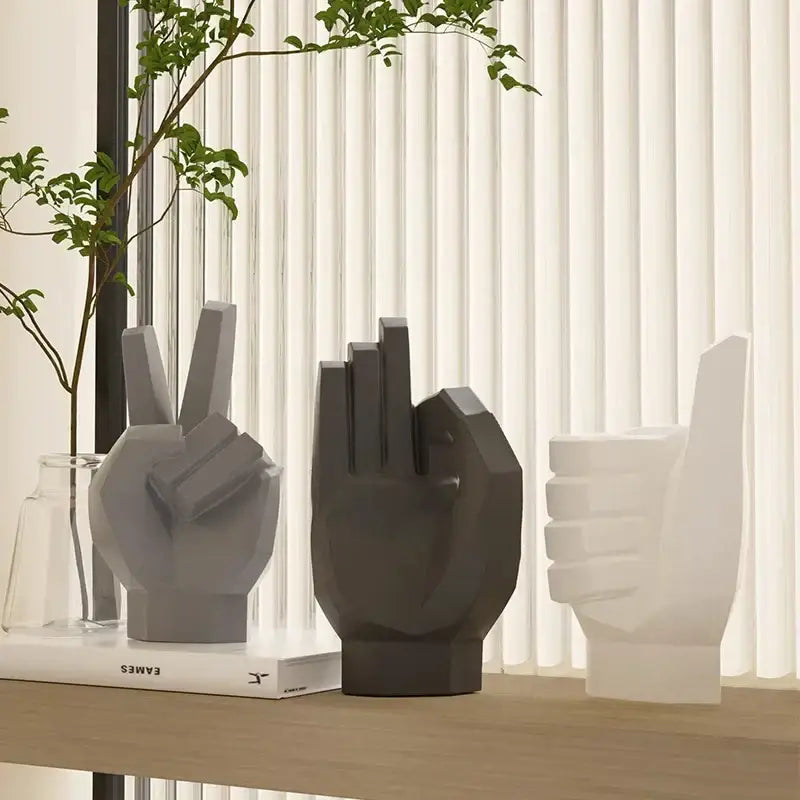 Three minimalist geometric hand sculptures in matte gray black and white for gesture art decor on a wooden shelf