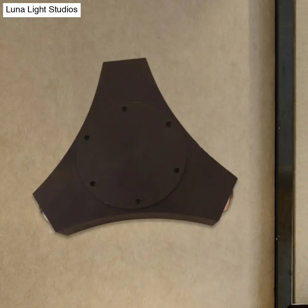 Dark brown triangular wall-mounted speaker with circular center and six holes paired with geometric metallic shade bronze sconce
