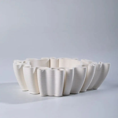 Geometric off white ceramic flower pot sculpture with sculpted petal design and vertical ribbed texture for living room decor