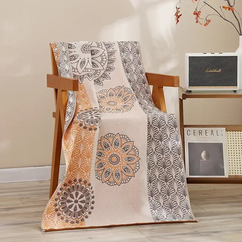 Beige throw blanket with intricate mandala and feather patterns in orange gray and black on wooden chair decorbites cotton bath towel accessory
