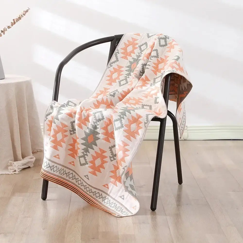 A soft cream-colored decorbites cotton bath towel with coral and gray geometric pattern draped on black chair
