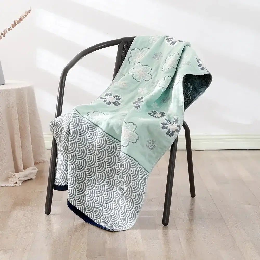 A soft mint green and gray decorbites cotton bath towel with floral and wave motifs draped over a black metal chair