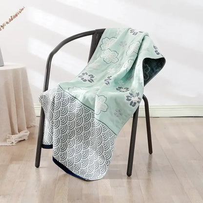 A soft mint green and gray decorbites cotton bath towel with floral and wave motifs draped over a black metal chair