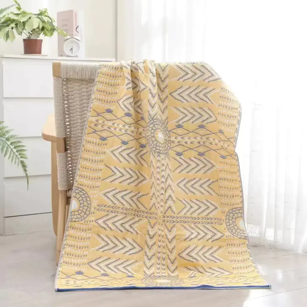 A soft yellow decorbites cotton bath towel with gray and navy geometric patterns draped on a woven chair