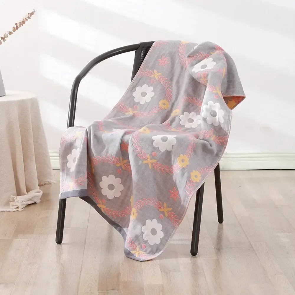 Gray floral-patterned decorbites cotton bath towel with white yellow and pink blossoms draped over a black chair