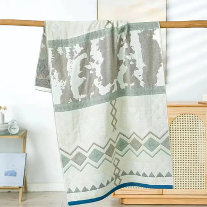 A soft off-white decorbites cotton bath towel with gray and teal geometric pattern and quilted texture on top edge