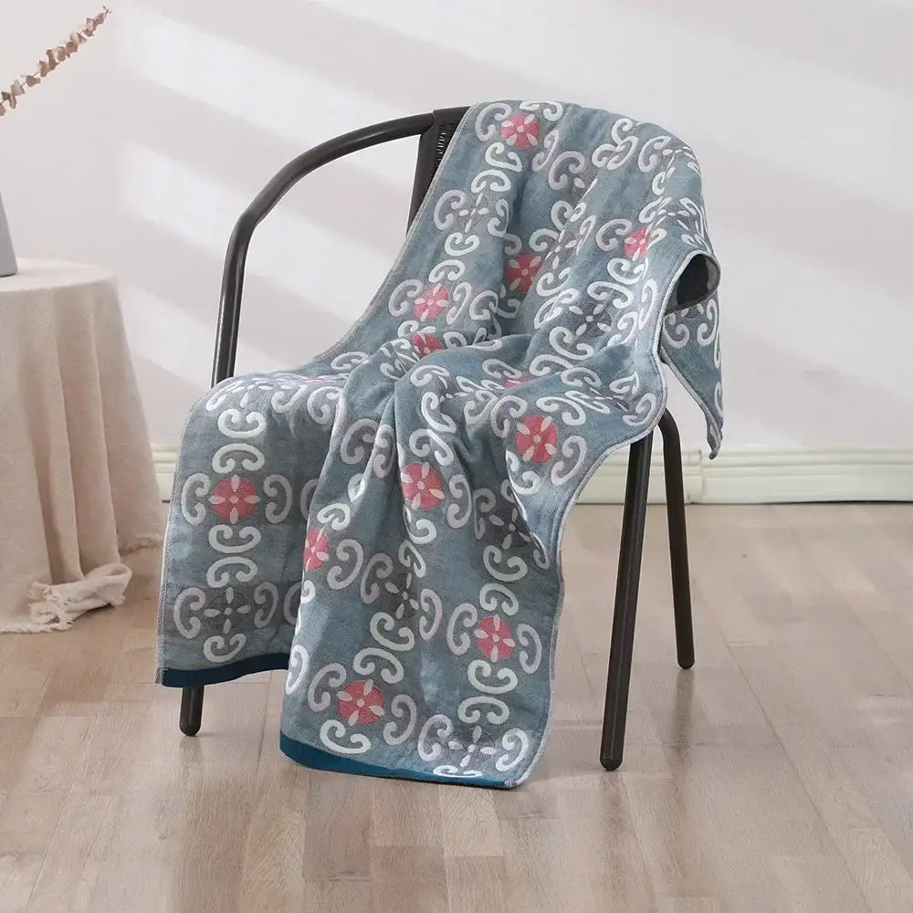 A soft plush blue decorbites cotton bath towel with pink and white floral motifs draped over a black chair