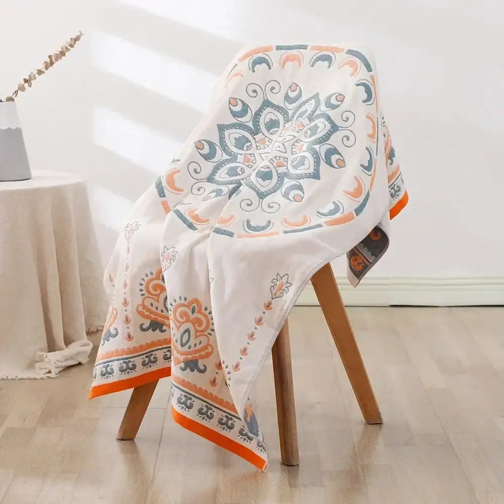 A soft white cotton bath towel with vibrant orange and teal mandala pattern draped on a wooden chair decorbites cotton bath accessory