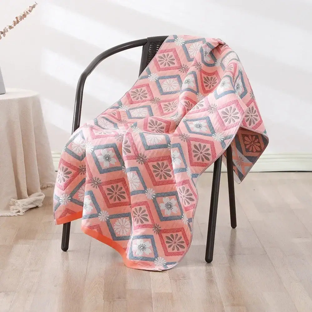 A soft pink and gray geometric-patterned decorbites cotton bath towel draped over a black chair for quick dry use