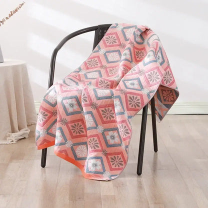 A soft pink and gray geometric-patterned decorbites cotton bath towel draped over a black chair for quick dry use