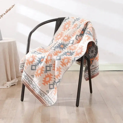 A cream-colored decorbites cotton bath towel with orange and gray geometric pattern draped over a black chair
