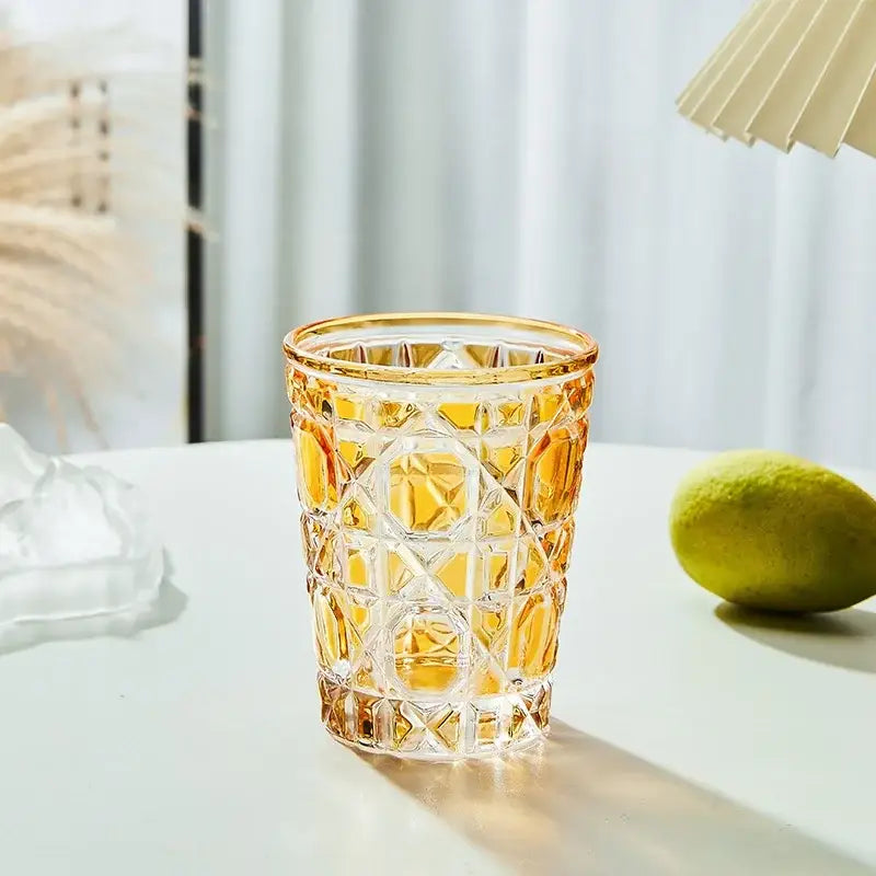 A faceted amber glass tumbler with geometric cut patterns and gold rim is a heavy whiskey glass for dining
