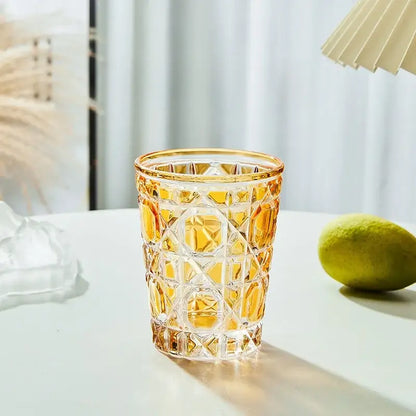 A faceted amber glass tumbler with geometric cut patterns and gold rim is a heavy whiskey glass for dining