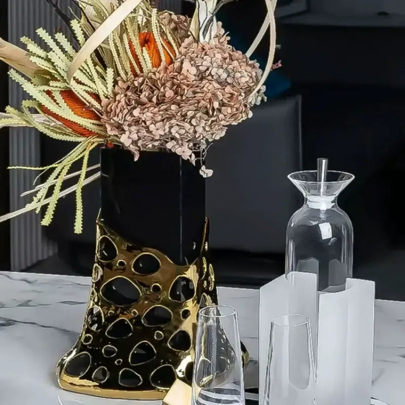 A sleek black and gold ceramic vase with a modern perforated design holding dried flowers complements decorbites geometric acrylic glass vase decor
