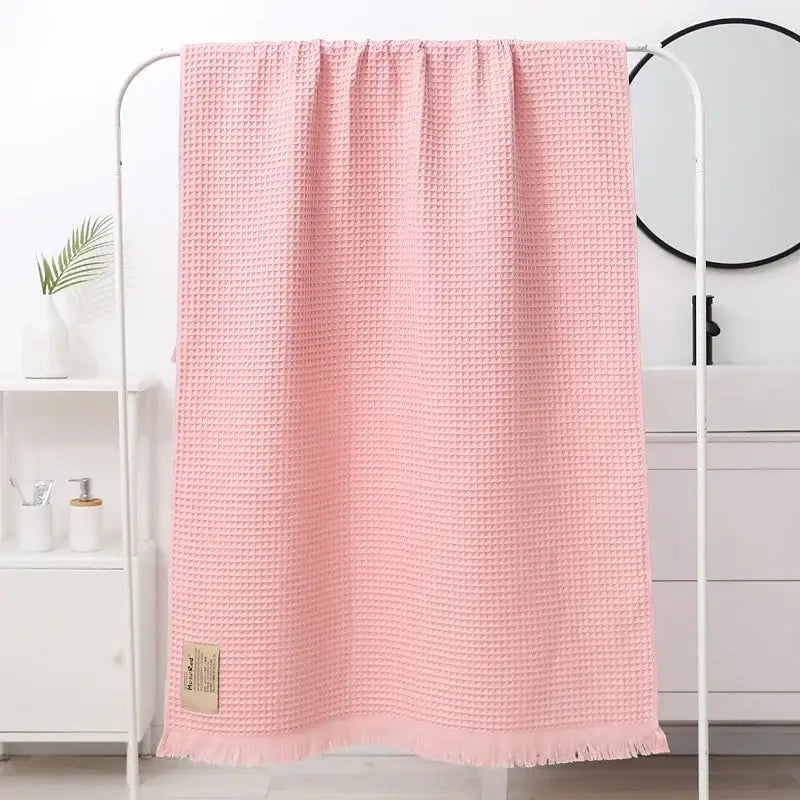 A soft pink bath towel with a waffle weave, fringed edge, and beige label from decorbites geometric tassel bath collection