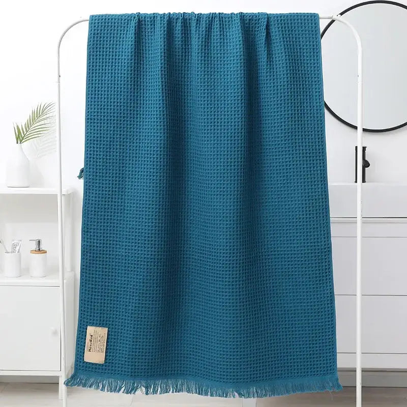 A teal-colored decorbites geometric tassel bath towel with waffle weave, fringed edge, and small beige label