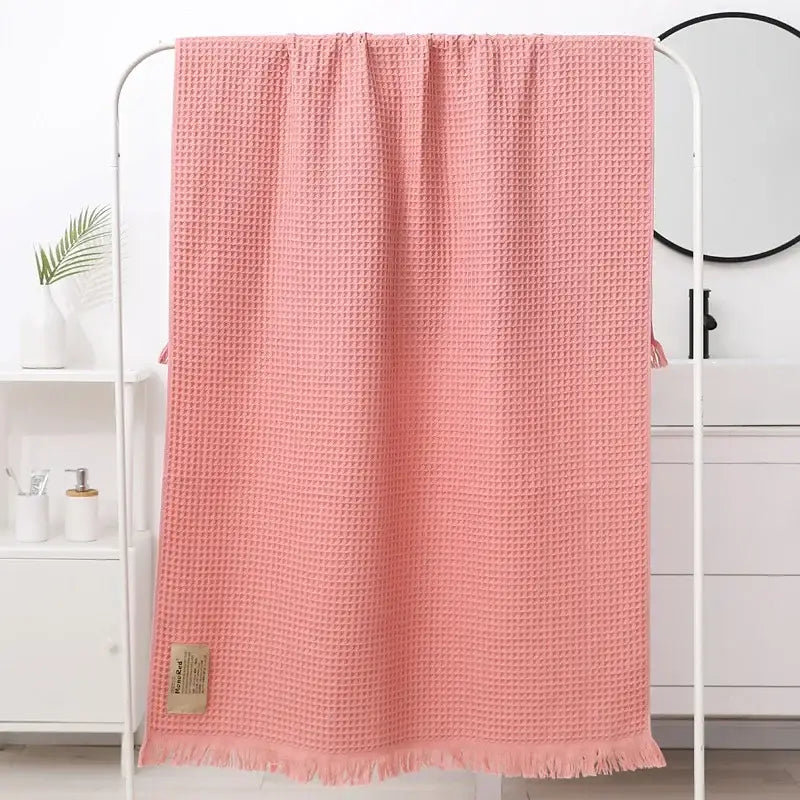 A soft pink waffle weave bath towel with frayed edges and beige label from decorbites geometric tassel bath collection