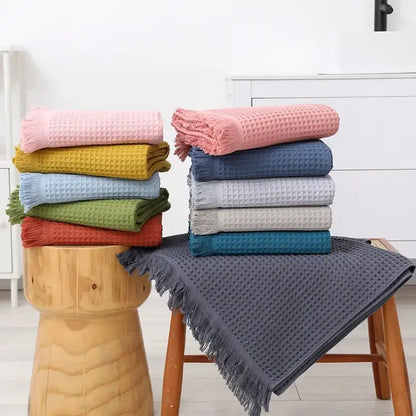 Stack of pastel and earth-toned decorbites geometric tassel bath towels in soft waffle cotton with fringed edges for bathroom decor
