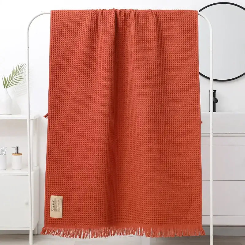 A terracotta-colored bath towel with a soft waffle weave and fringed edges from decorbites geometric tassel bath collection