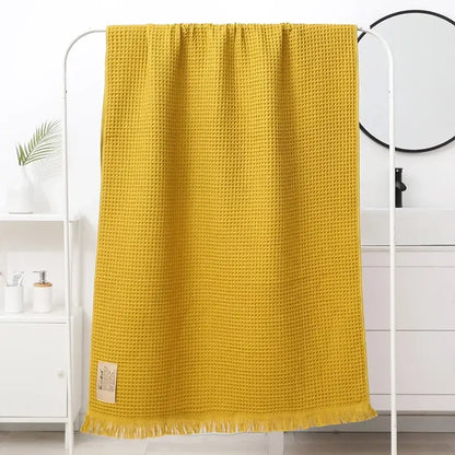 A vibrant yellow bath towel with soft waffle weave texture and fringed edges from decorbites geometric tassel bath collection