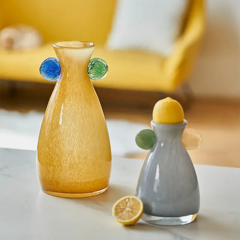 A translucent amber decorbites geometric glass vase with textured surface and colorful blue and green handles beside a gray lemon squeezer