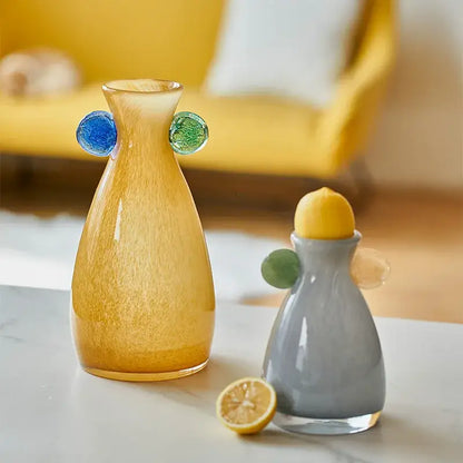 A translucent amber decorbites geometric glass vase with textured surface and colorful blue and green handles beside a gray lemon squeezer