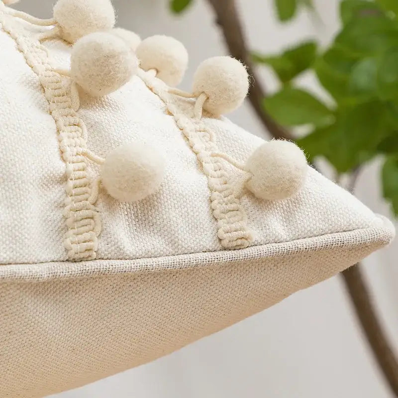 Cream-colored pillow cover with textured fabric and decorative pom-poms featuring decorbites geometric tufted design