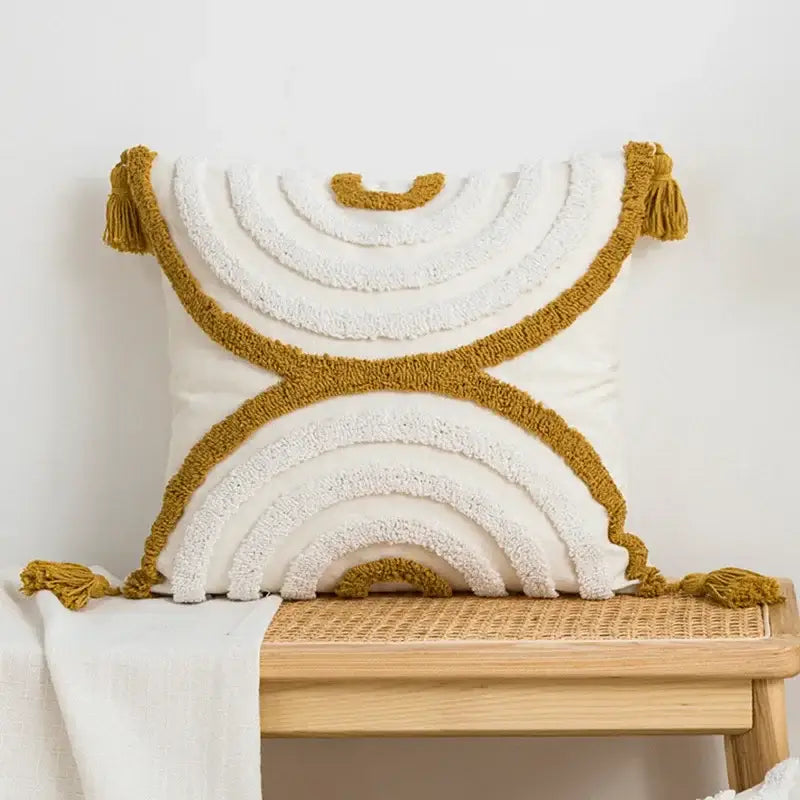 Cream-colored cushion cover with geometric tufted plush layered rainbow design in mustard and white yarn with tassels
