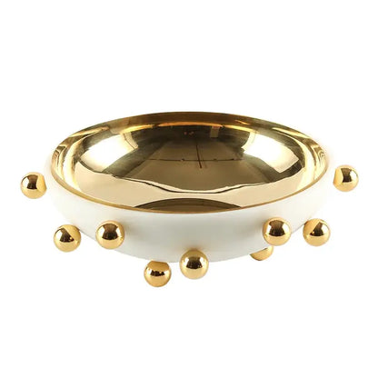 A sleek white ceramic fruit bowl round with polished gold interior and decorative gold studs on rim