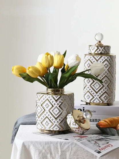 White ceramic decorative jar with golden relief geometric pattern and crystal knob holding yellow and white tulips