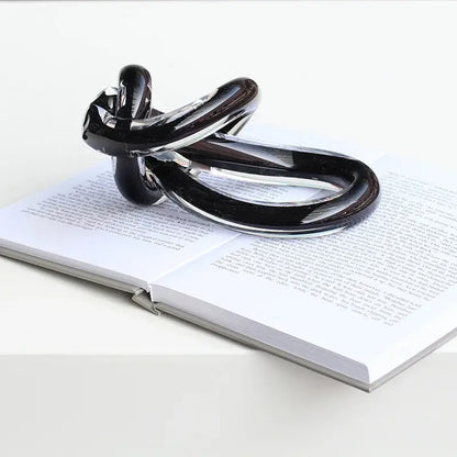Shiny black glass twine knot sculpture with sleek intertwined design resting on open book for home decor