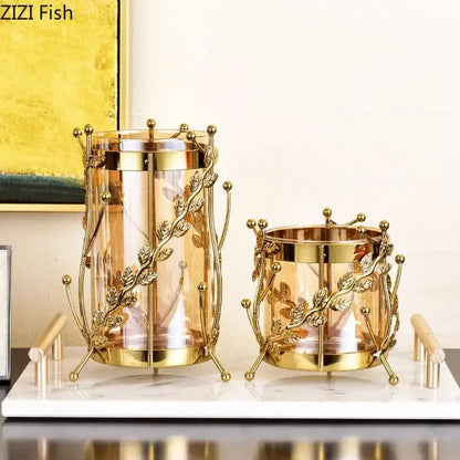 Gold-toned metal candle holders with clear glass inserts featuring intricate gilded tree branch leaf designs for living room decor