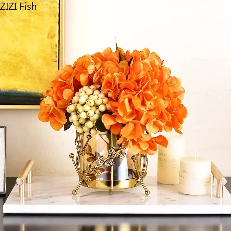 Golden metallic gilded tree branch glass vase with intricate leaf design holding vibrant orange hydrangea bouquet