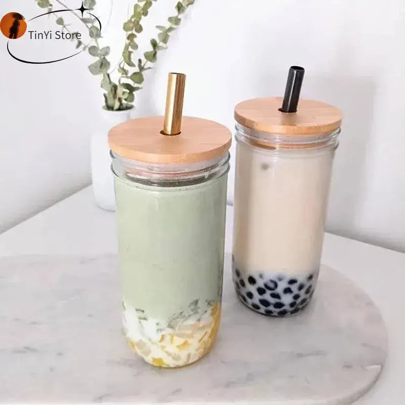 Two clear decorbites glass boba smoothie cups with bamboo lids and stainless steel straws holding matcha and milk tea