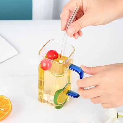 A clear decorbites glass drinking cup with a vibrant blue handle and citrus decor filled with a golden beverage