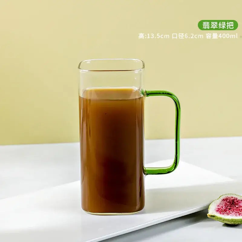A clear glass drinking cup with a jade green handle filled with a rich brown beverage by decorbites