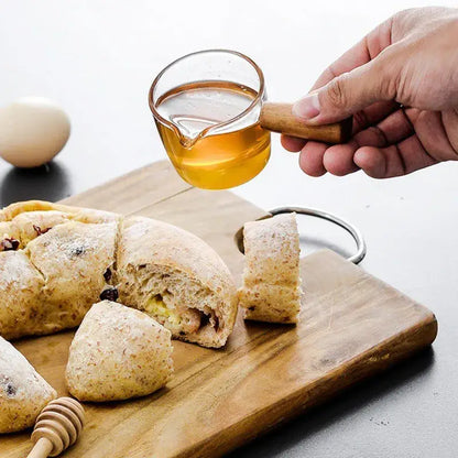 A clear glass espresso measuring cup with wood handle filled with golden amber honey for kitchen use