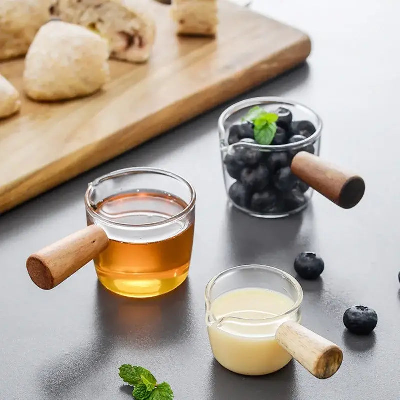 Three clear glass espresso measuring cups with wood handles filled with different liquids and garnished with mint leaves