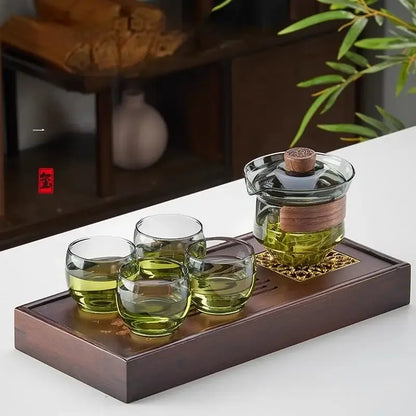 Clear glass gaiwan cup set with wooden lid handle and four cups on a dark wood tray for dining room tea filtering