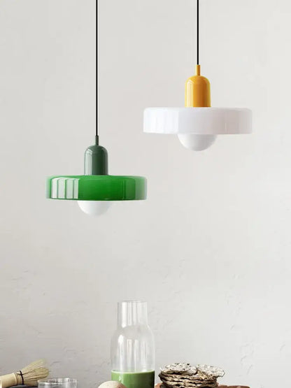 Modern glass pendant lighting with glossy green and yellow ceramic shades suspended by black cords in bauhaus style
