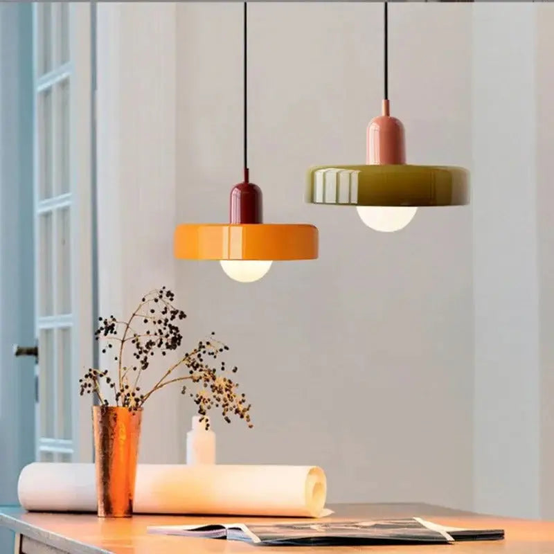 Two glass pendant lighting fixtures with glossy orange and olive green circular shades hang above a wooden table