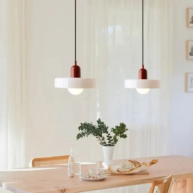 Two modern glass pendant lighting fixtures with matte white shades and red cylindrical details in Bauhaus style