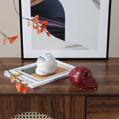 A glossy white ceramic pumpkin decor with marbled texture and dark stem resting on a magazine for abstract melting apple decorbites