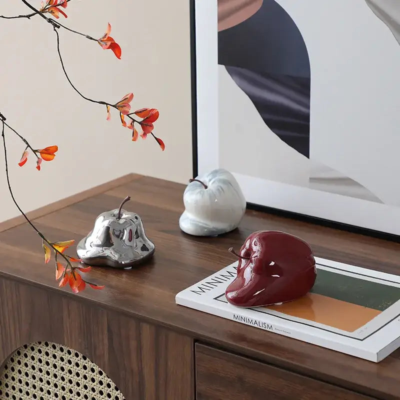 A glossy red abstract melting apple ceramic sculpture with a small stem sitting on a magazine for living room decorbites decor