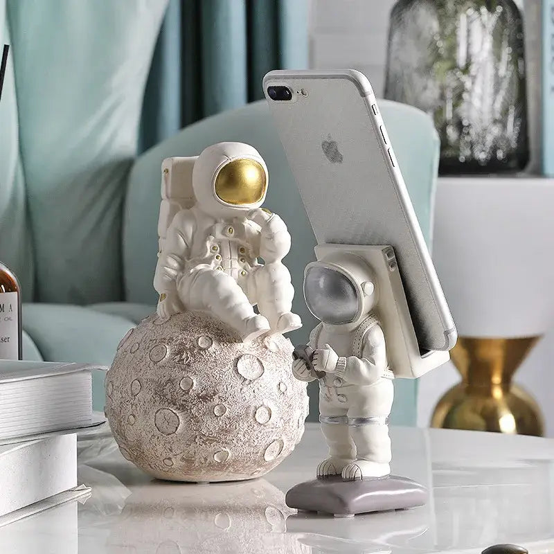 Glossy white and gold astronaut phone holder figurine seated on textured moon surface for bedroom decor