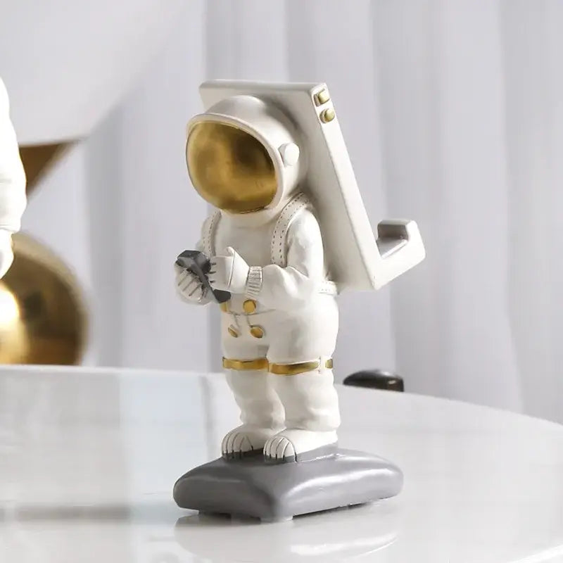 Glossy white and gold astronaut phone holder figurine with gold visor standing on gray base for bedroom decor